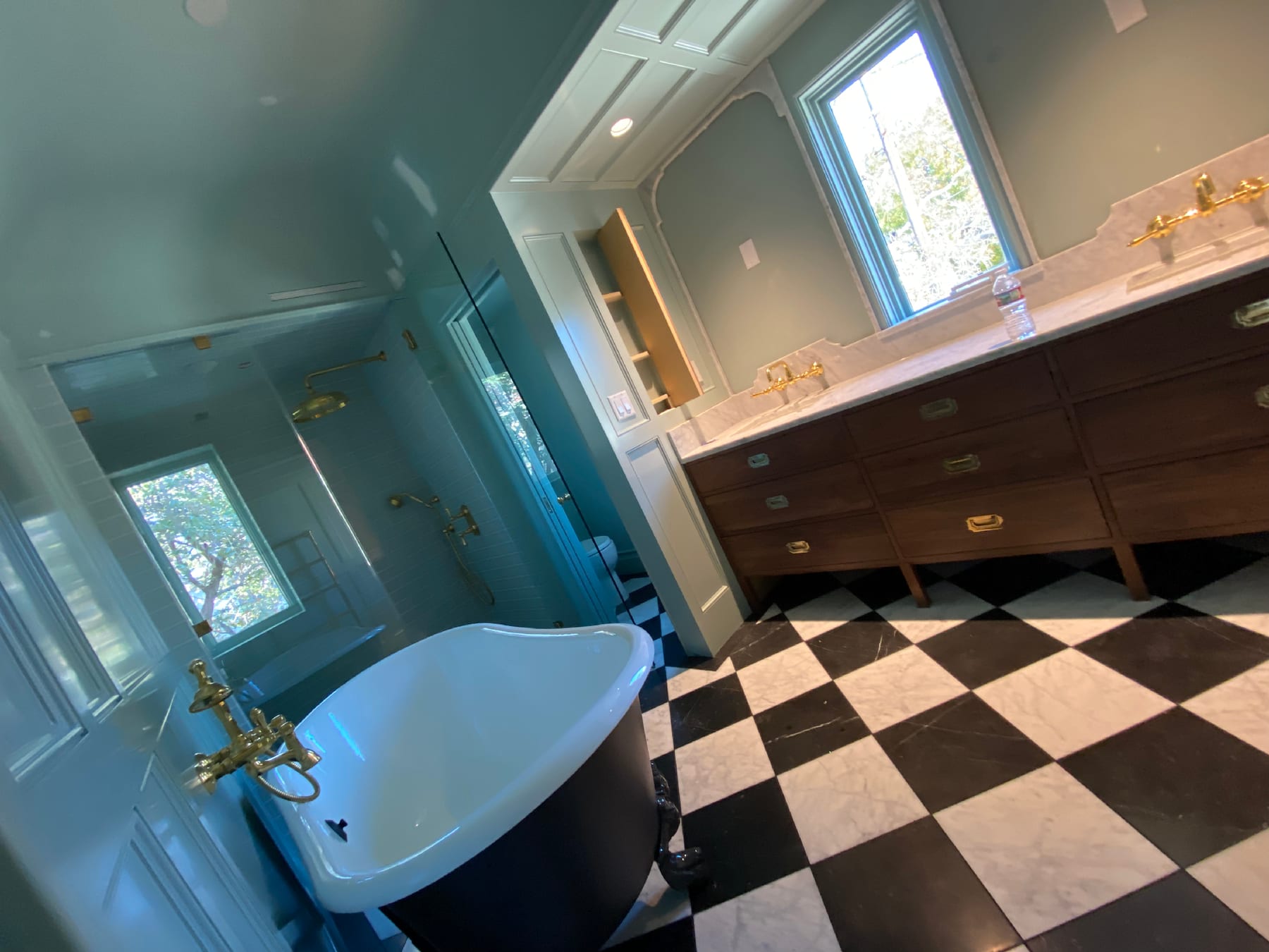 Corner of a sage-walled master bath: clawfoot tub, glass shower, walnut vanity, and a checkered marble floor.