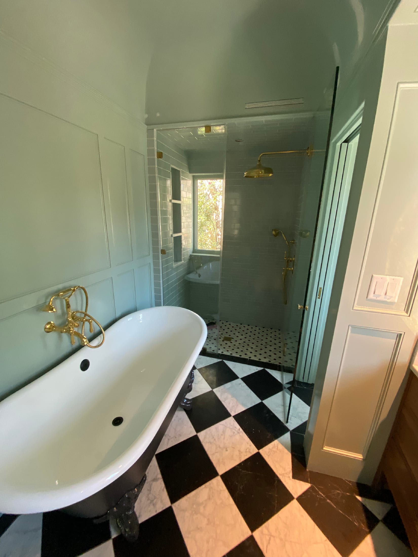 Master bath with a clawfoot tub, brass fixtures, and a glass walk-in shower lined in soft blue subway tile over a basketweave marble floor.