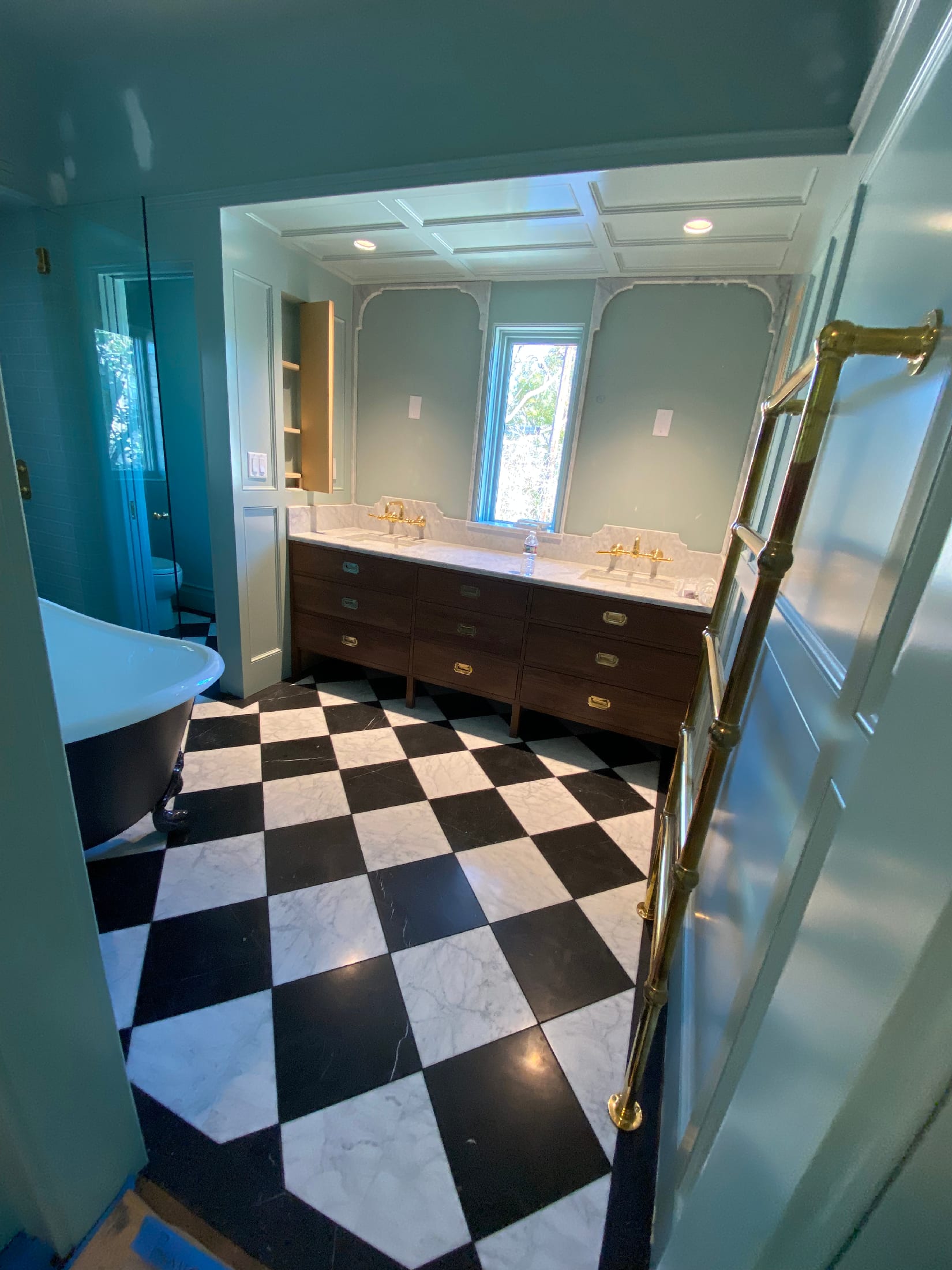Walnut double vanity with marble counters and a brass towel ladder over a black-and-white checkered marble floor.