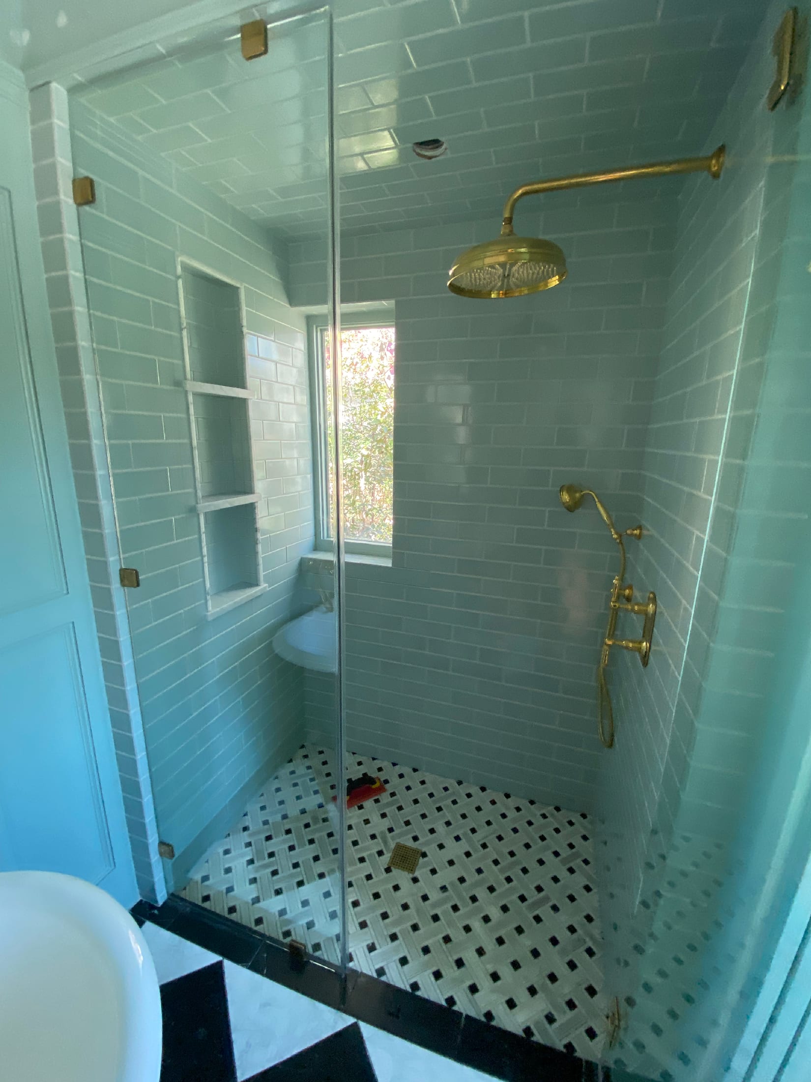 Walk-in shower with soft blue subway tile walls, a recessed niche bench, brass fittings, and a basketweave marble shower floor.