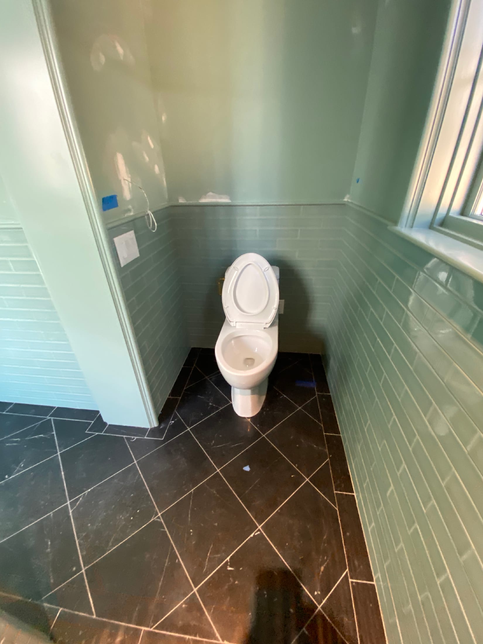 Powder room corner with light blue glass subway wainscot, sage walls, and a dark slate diagonal floor.