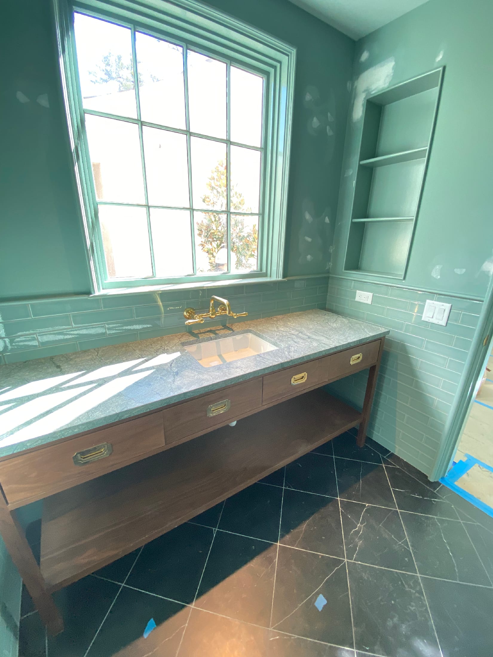 Walnut vanity with a polished stone counter and dark slate floor under a tall window.