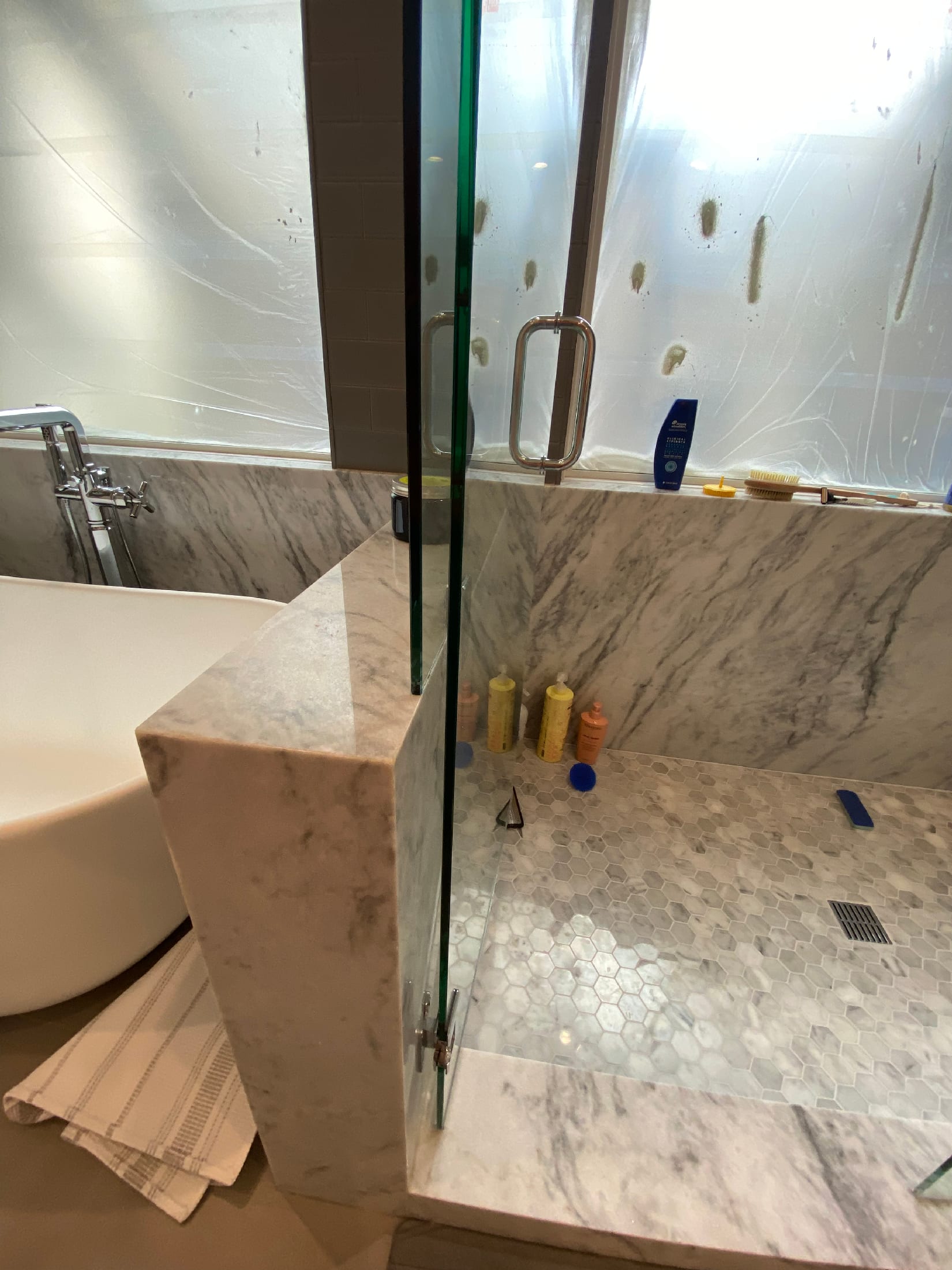 Carrara marble shower kerb and glass enclosure with gray subway tile walls and a hex marble pan.