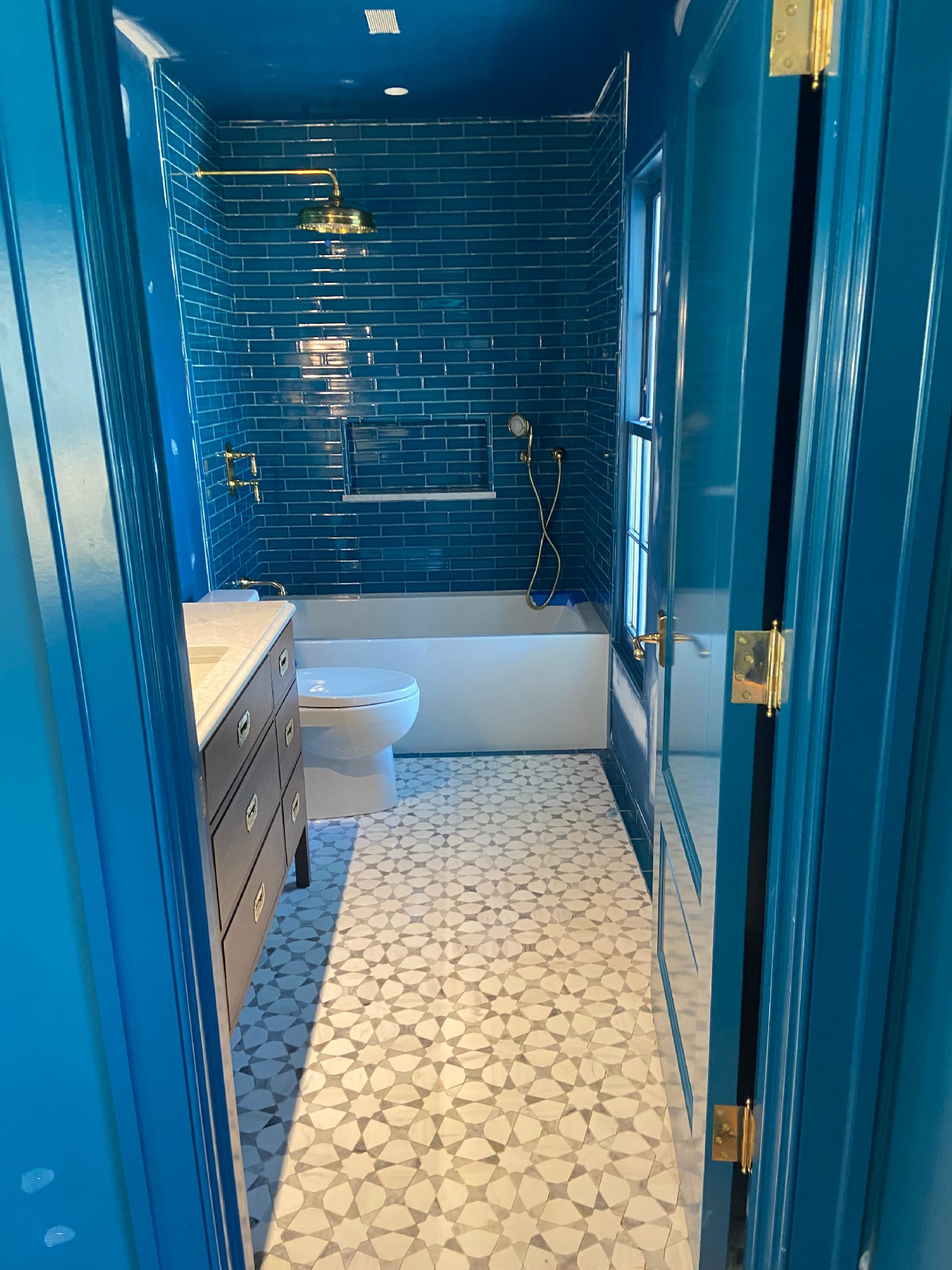 Detail of a cobalt bath: dark blue subway tile shower wall meeting a black, white, and gray mosaic floor.