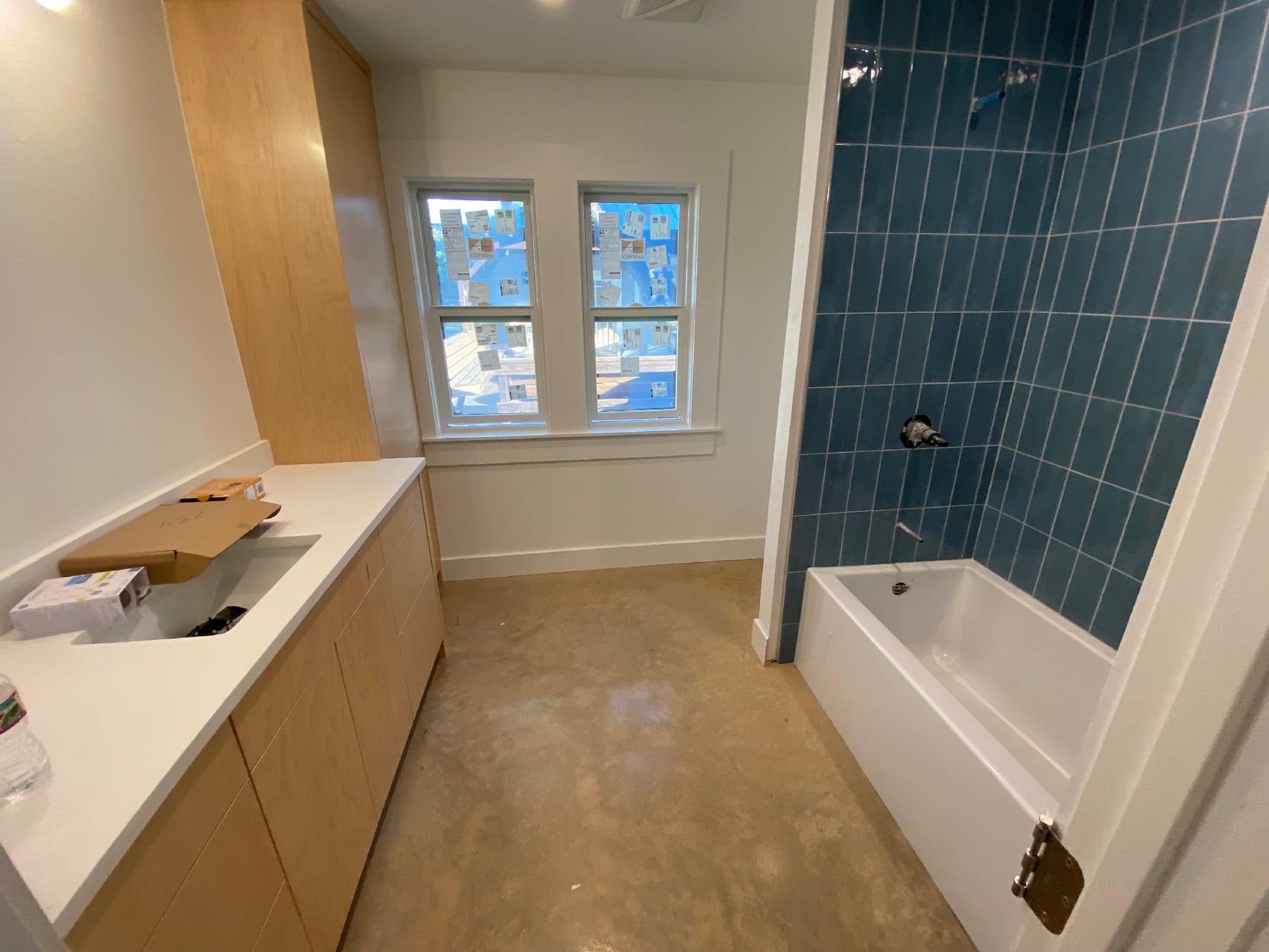 Modern bath with a vertical stacked blue tile tub surround, light wood vanity, and a polished concrete floor.