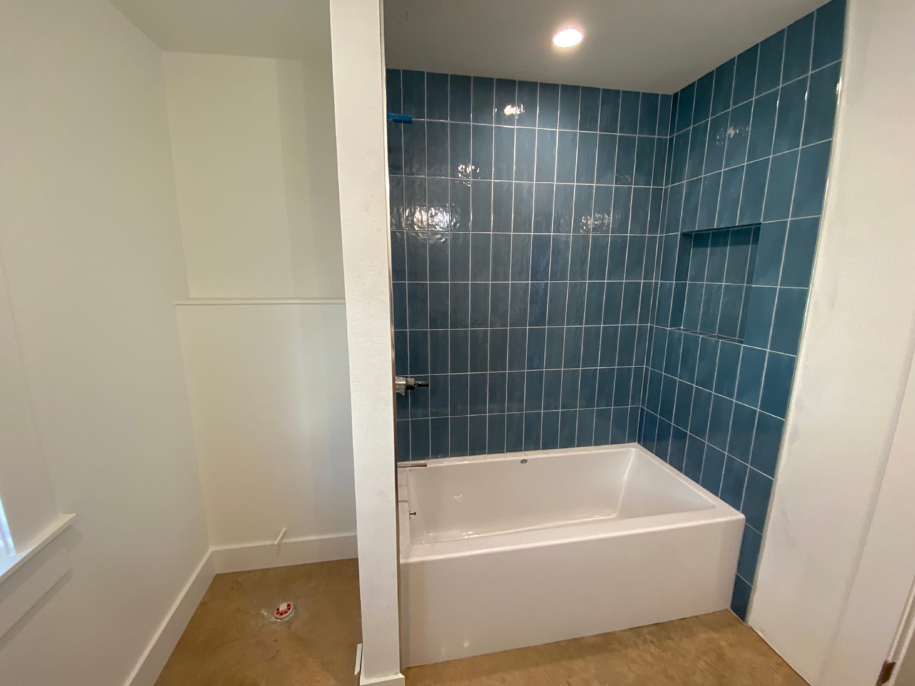 Vertical stacked blue tile tub surround with a recessed niche, set against a smooth concrete floor.