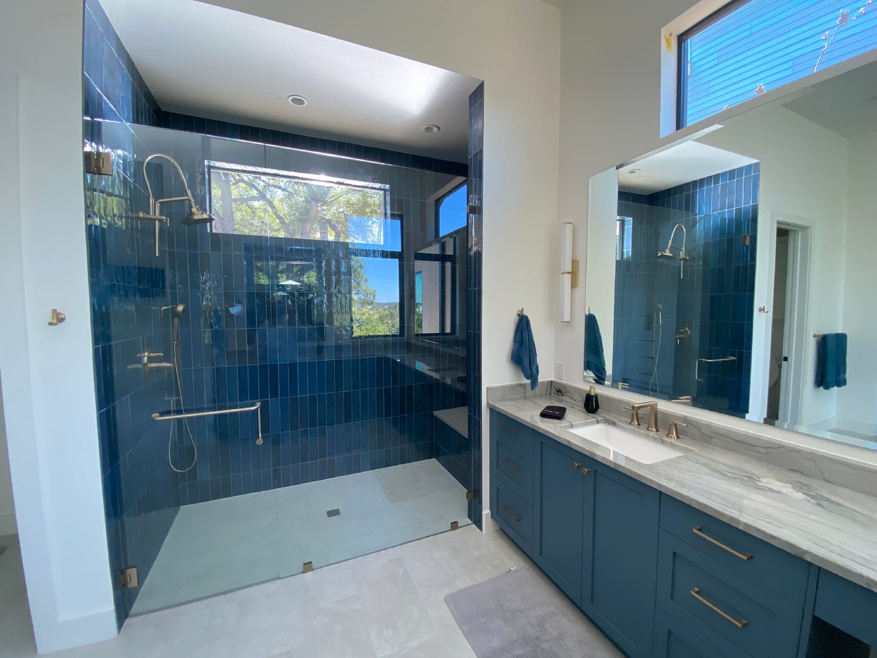 Walk-in shower in deep navy stacked tile with brass fixtures, framed by a navy vanity and large-format gray floor.
