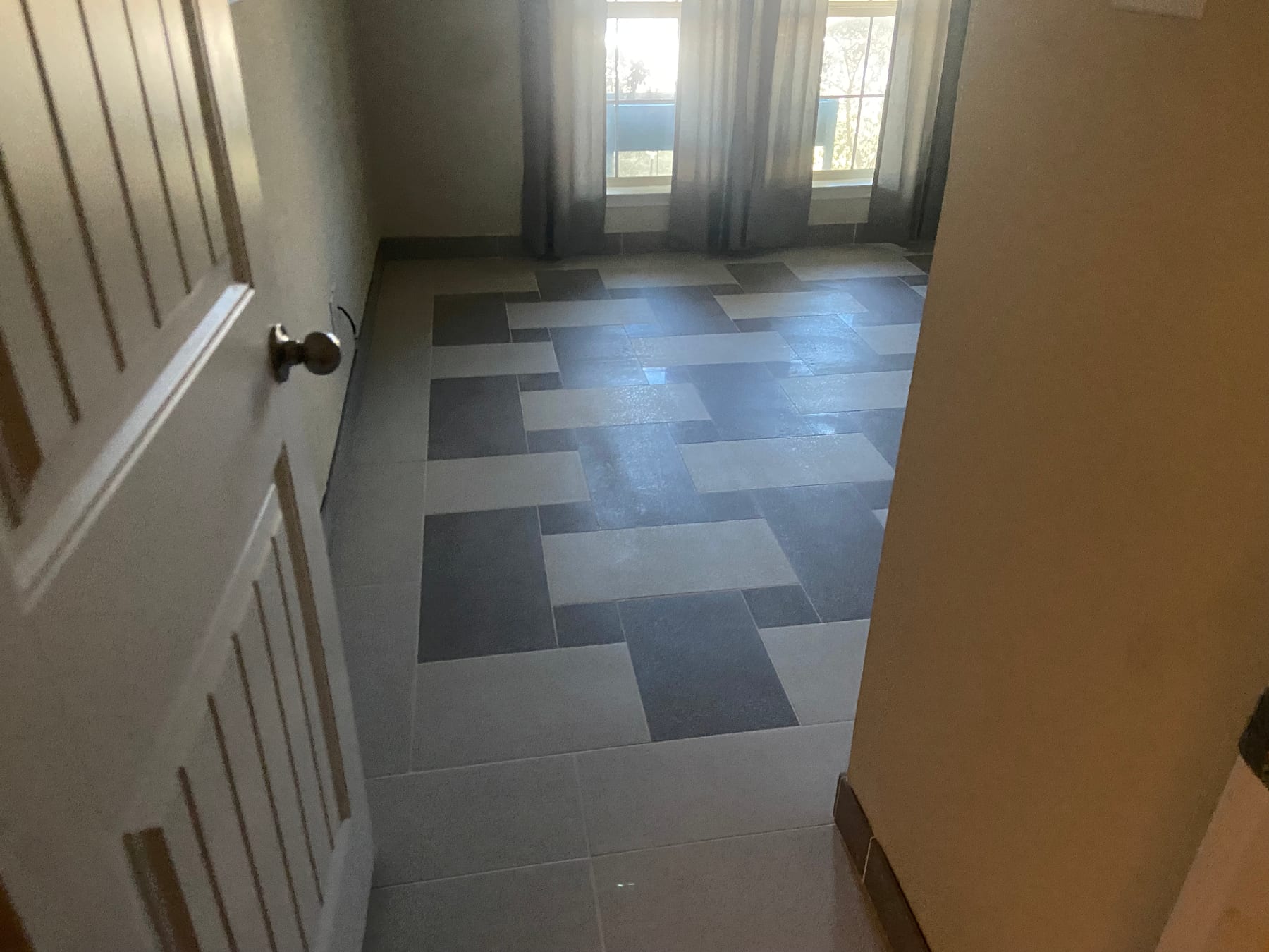 Hallway with a two-tone gray and cream basketweave tile floor leading toward sunlit windows.